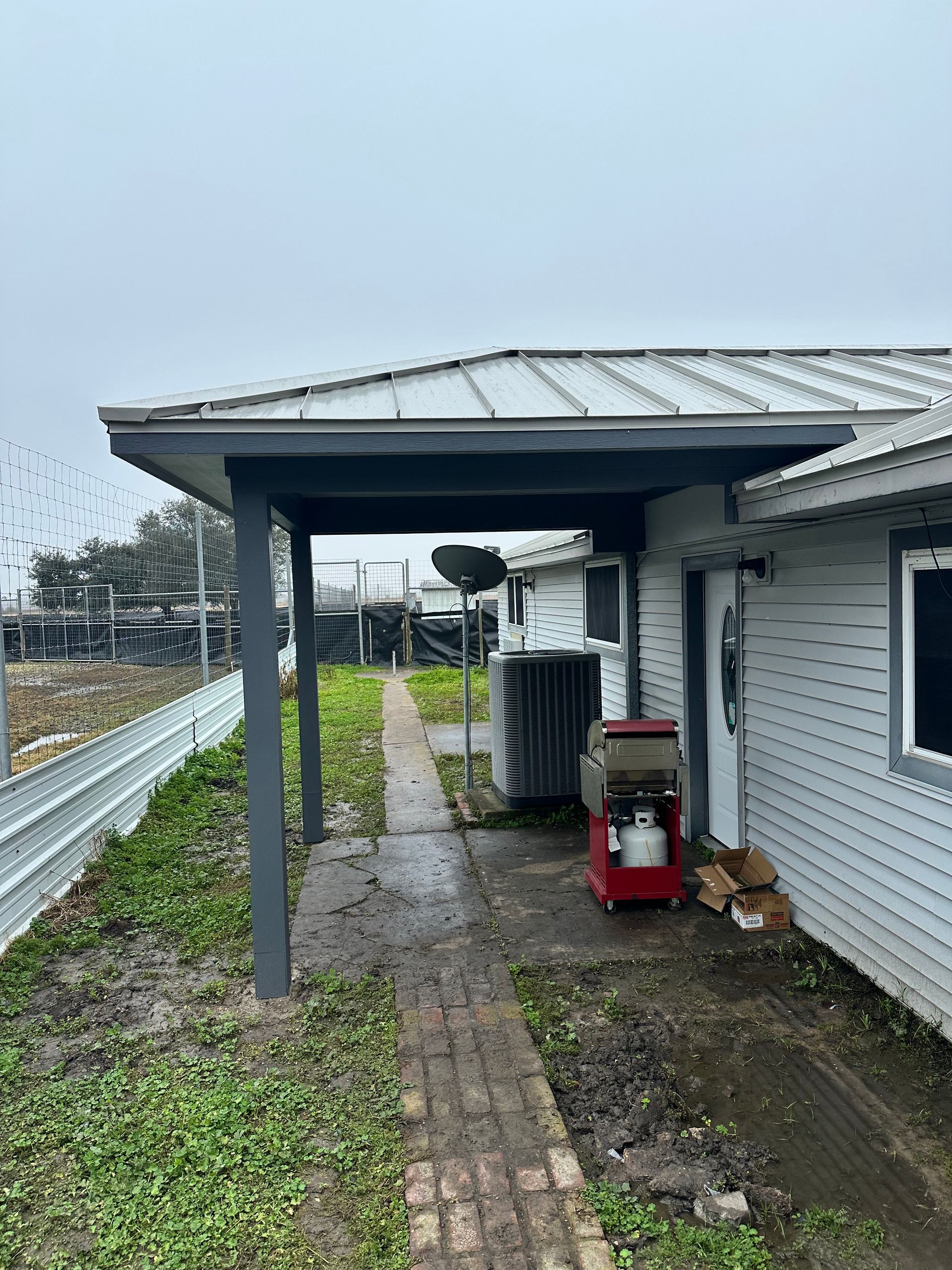 Covered walkway next to a building on a cloudy day. A red machine and AC unit are visible.