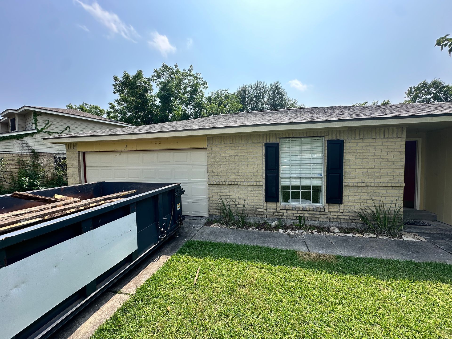 A one-story brick house with a dumpster in the front yard; blue sky.
