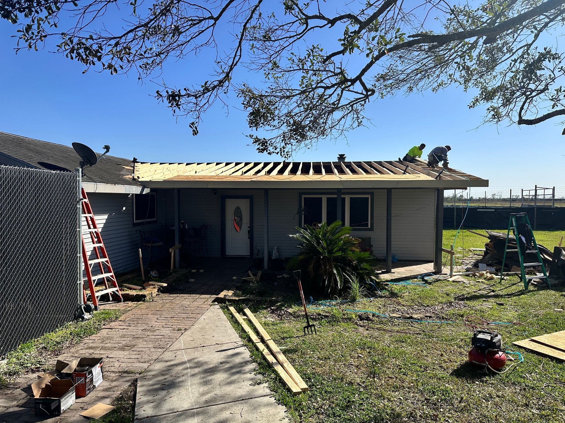 House with roof being rebuilt, workers on roof, ladders, blue sky.