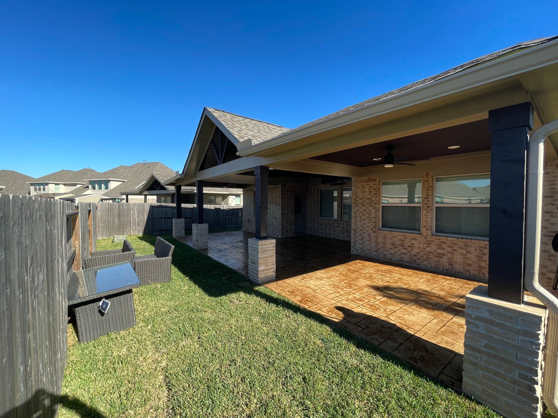 Backyard patio with brick and wooden columns, covered seating area, and green grass.
