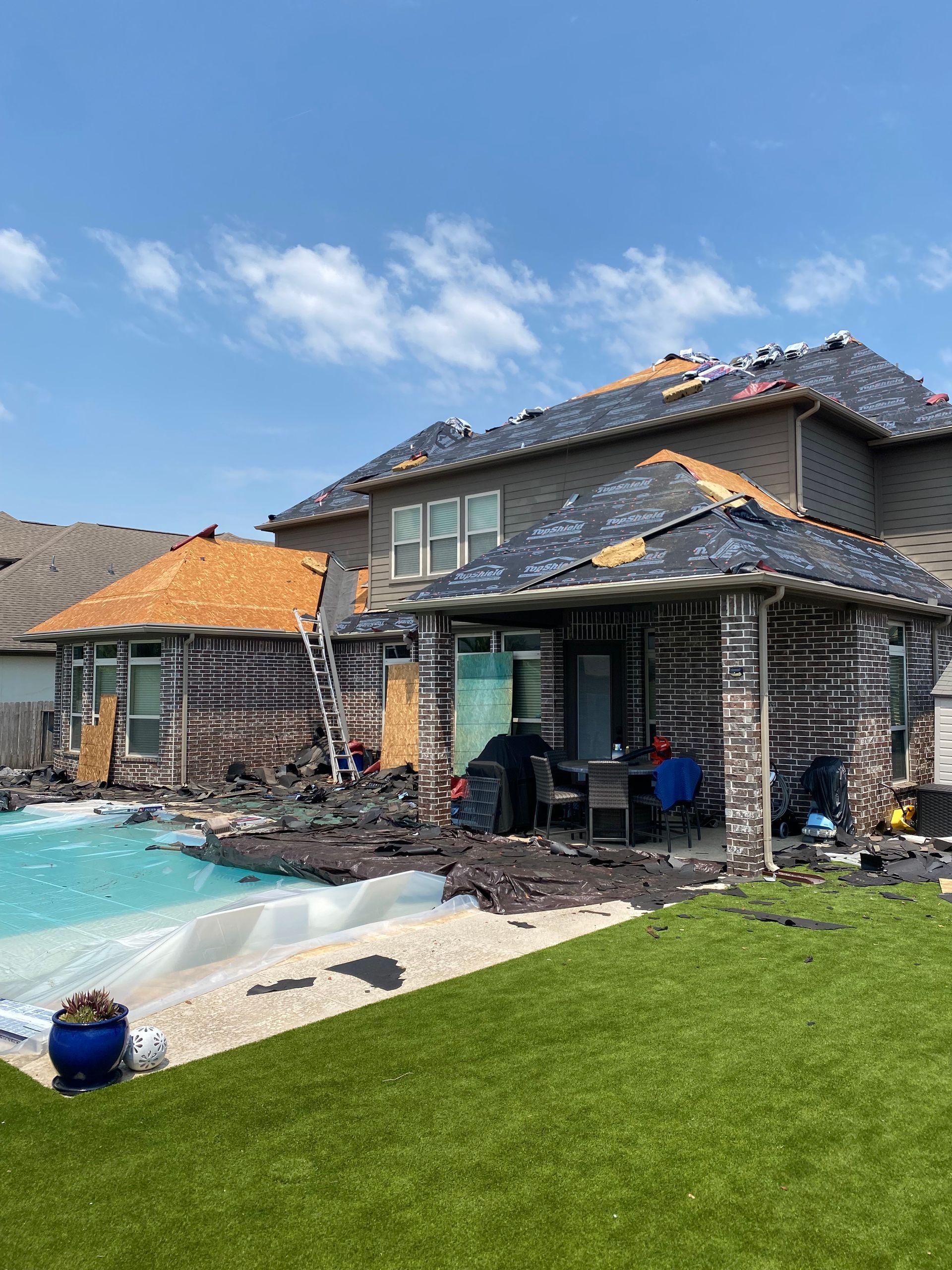 Backyard view of a house damaged by fire, with a pool and artificial turf lawn.