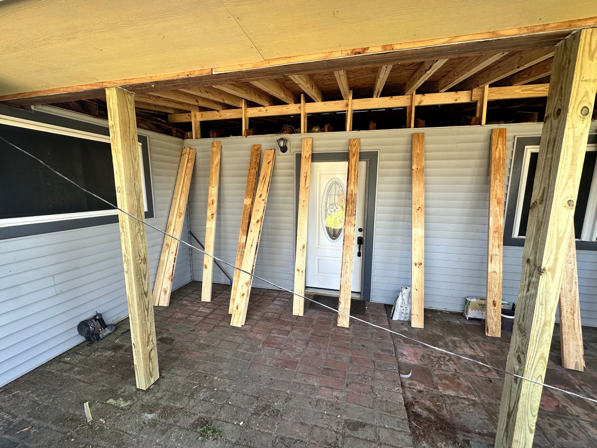 Porch roof and supports under construction. Gray siding, white door. Wooden beams propped up.