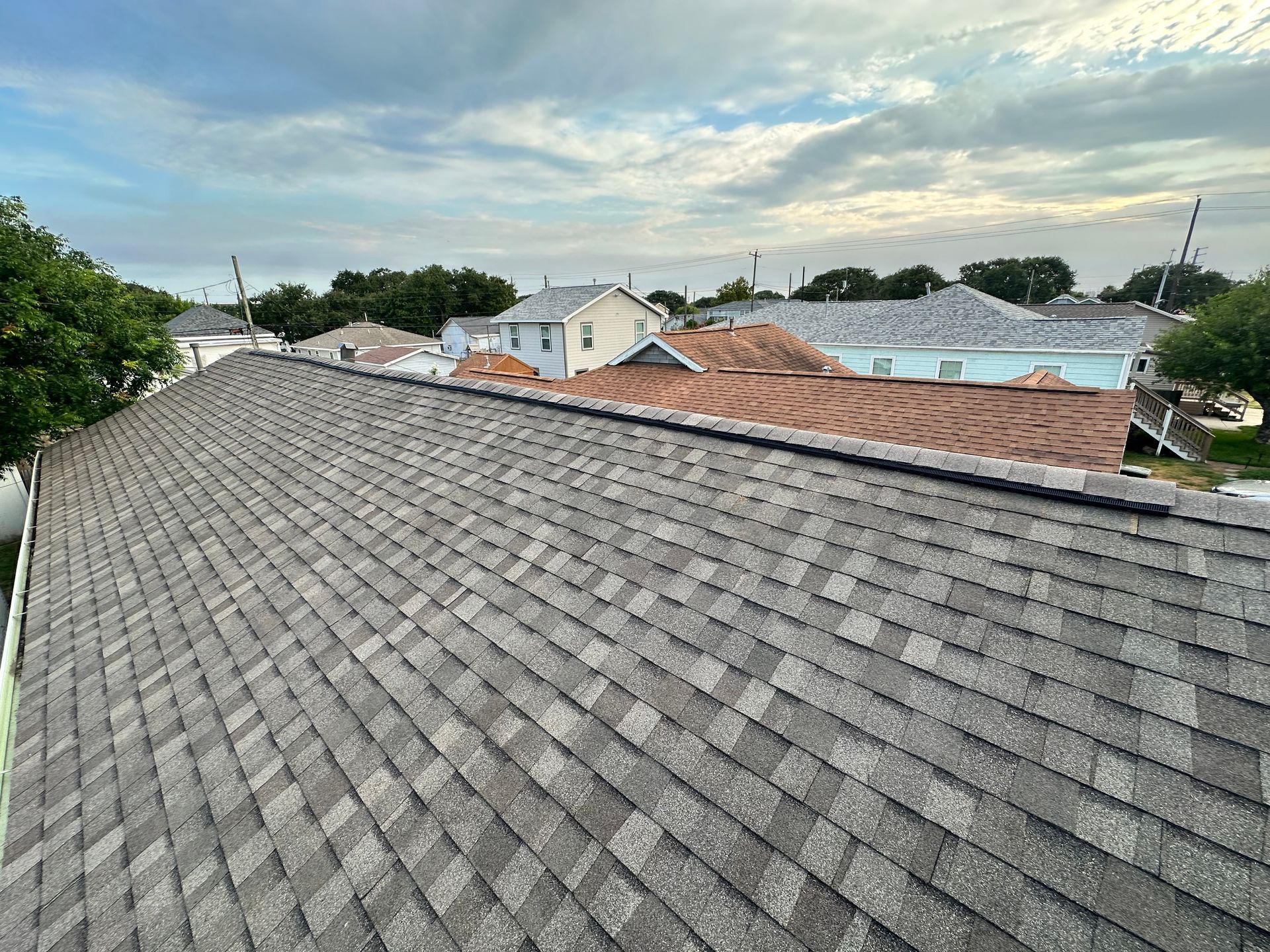 Gray shingled roof with a view of residential rooftops under a cloudy sky.