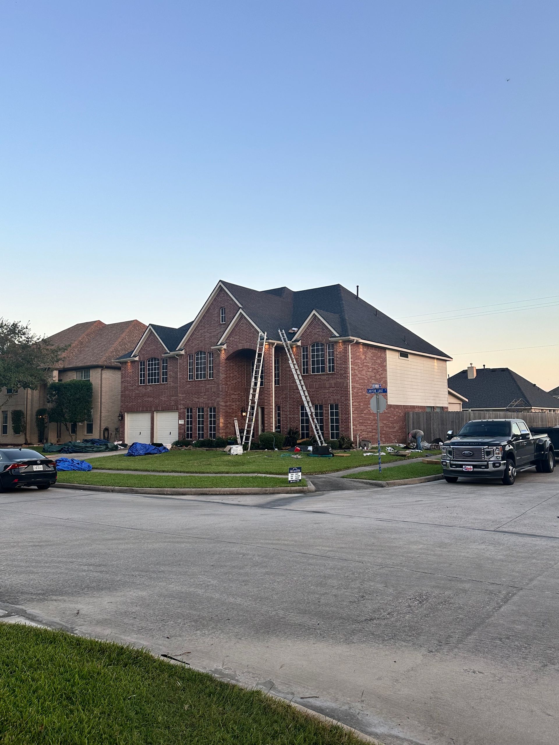 Brick house with ladder leaning against it; two cars and a truck parked outside.
