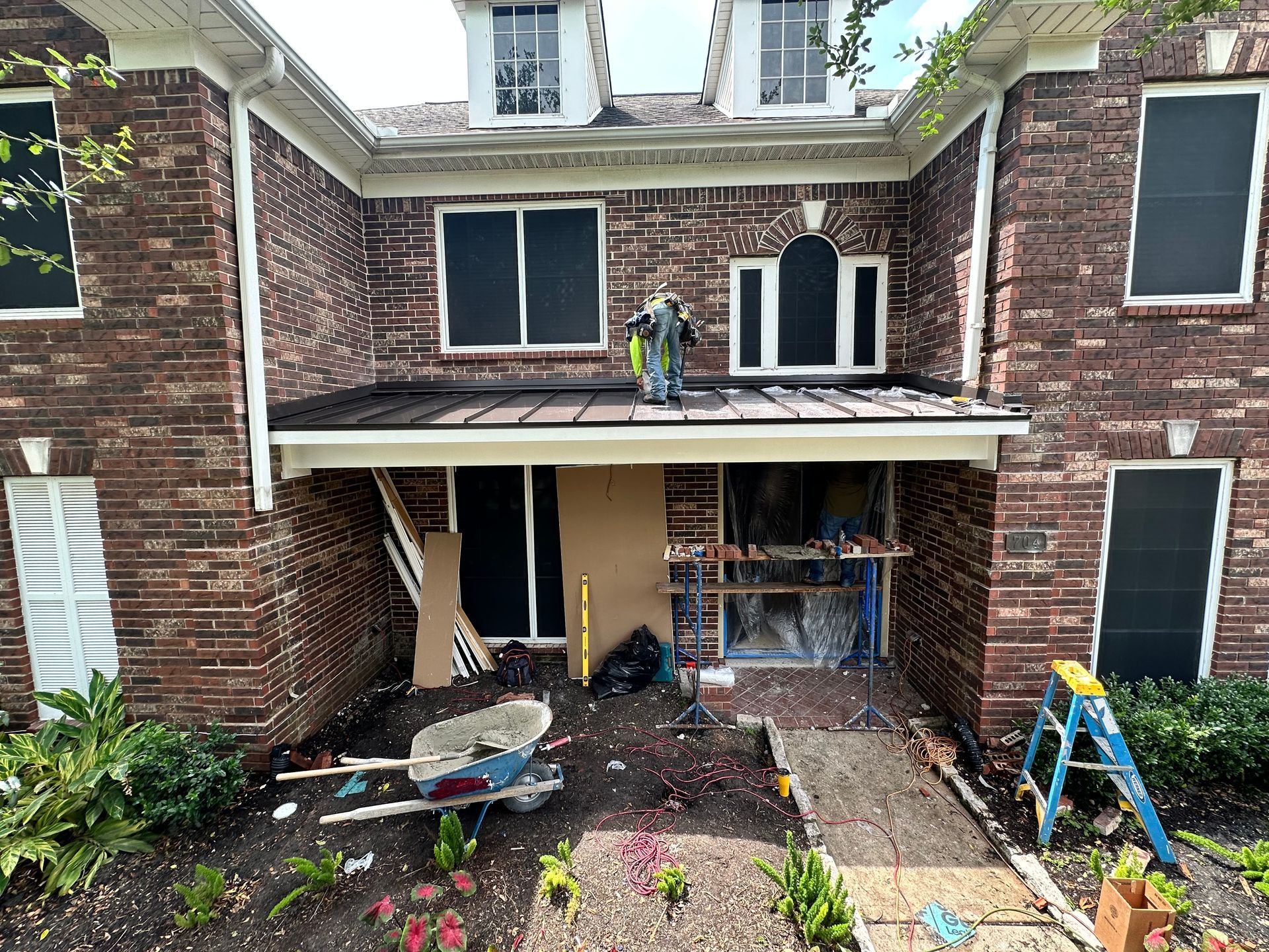 Brick house exterior under construction, with open doorway, debris, and a person on the roof.