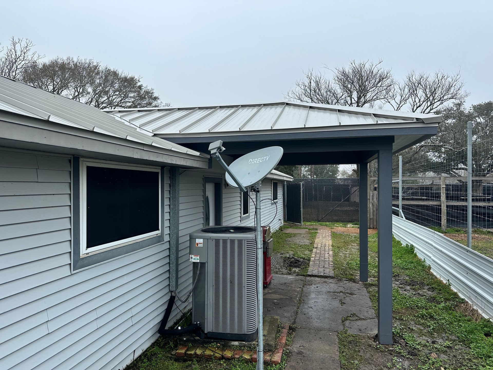 Side of a light blue house with a covered porch. A satellite dish is attached, and an AC unit is visible.