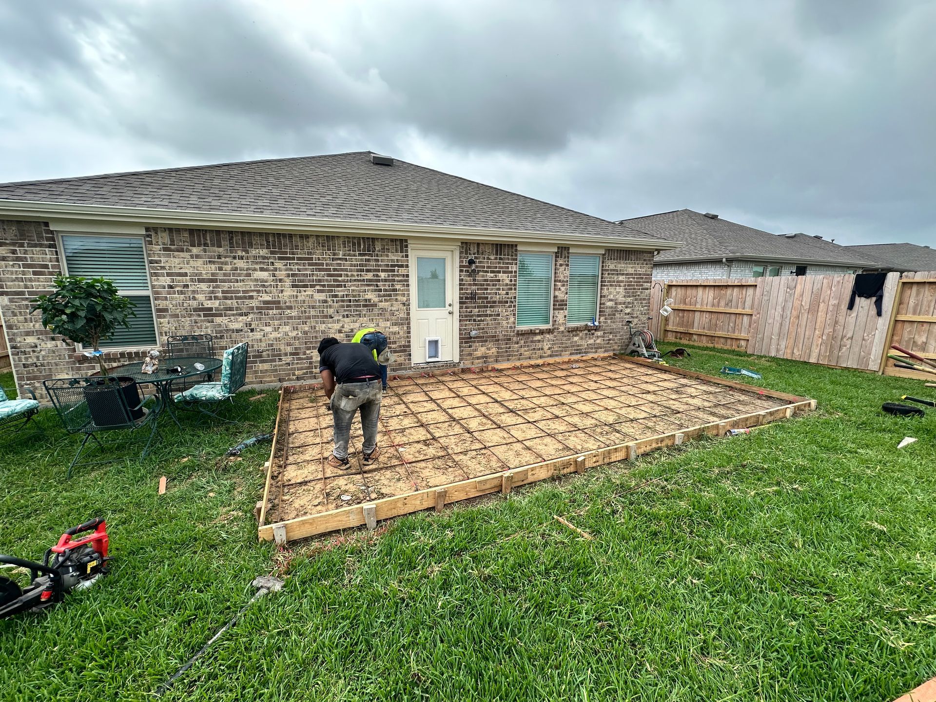 Person working on a concrete patio in a backyard with a cloudy sky.