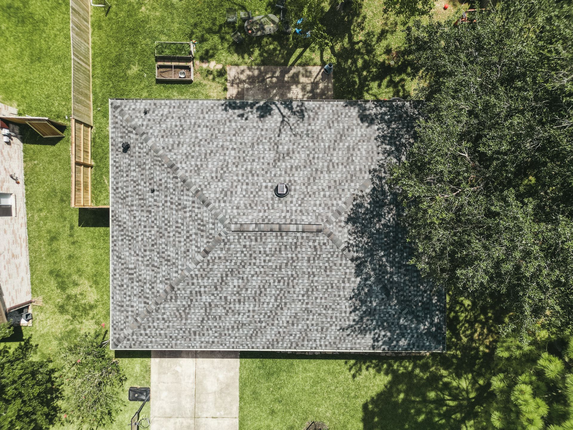 Overhead view of a house with a gray shingle roof, surrounded by green grass and a large tree.