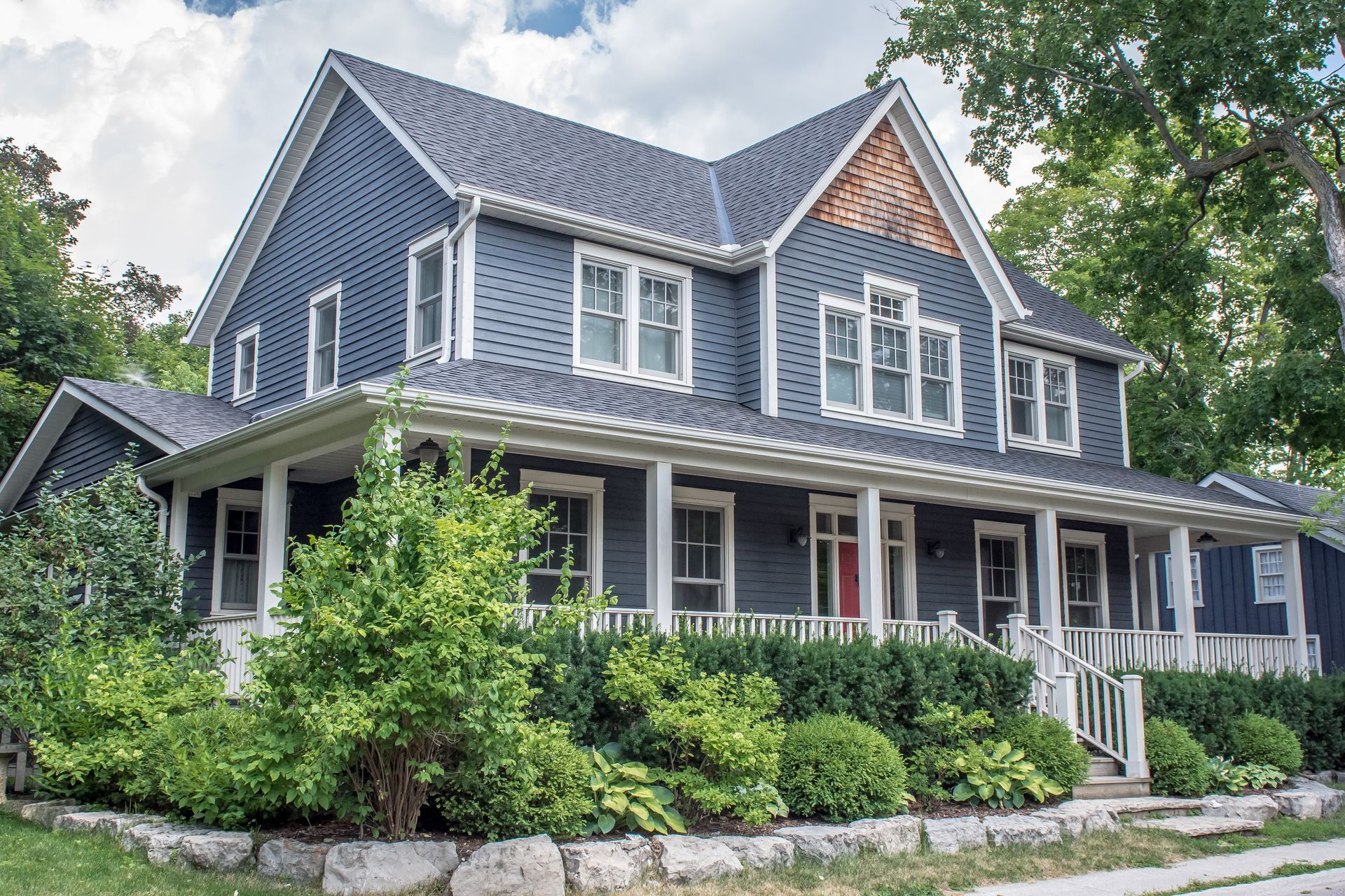 Blue two-story house with white trim, porch, and a lush green garden.