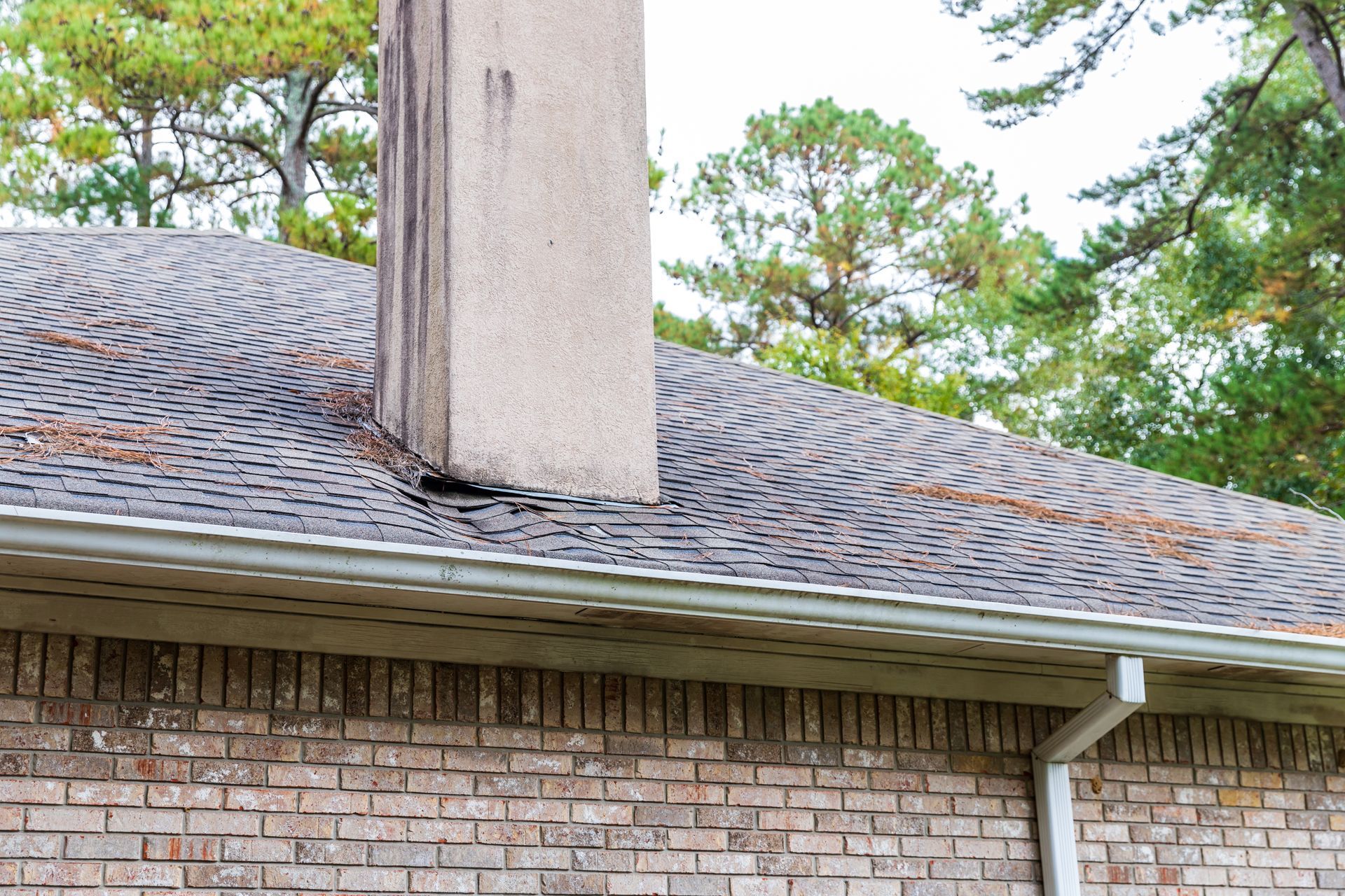 Brick building with chimney on roof, showing roof damage and a gutter.