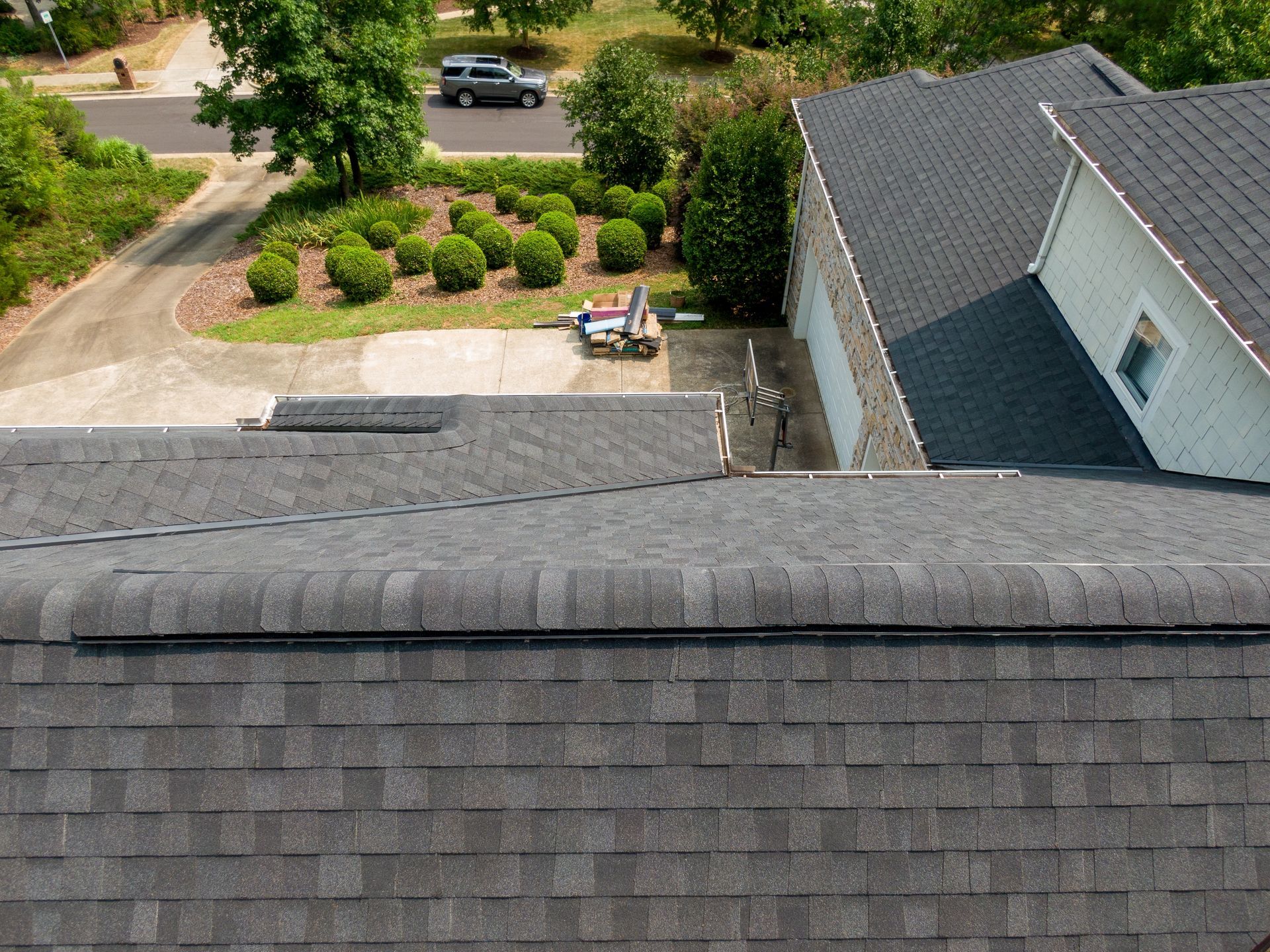 Overhead view of a house with a dark gray shingle roof and a driveway in a residential area.