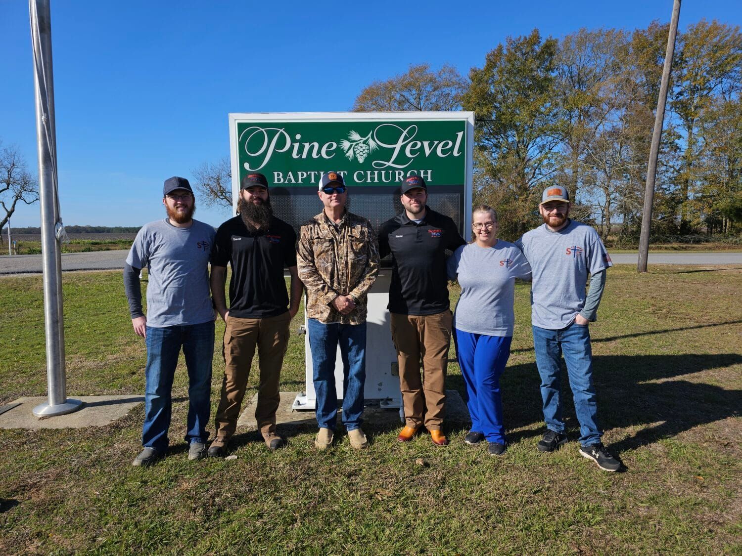 A group of people are standing in front of a sign that says pine level baptist church.