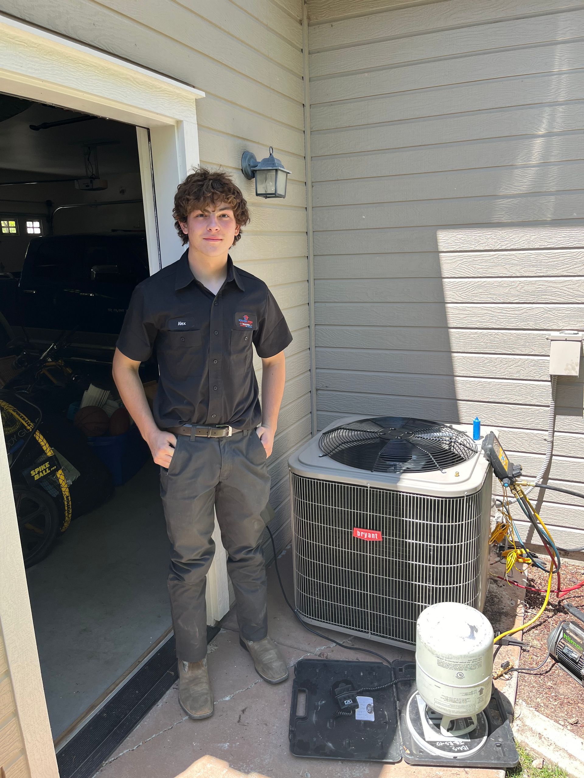 A young man is standing in front of an air conditioner in a garage.