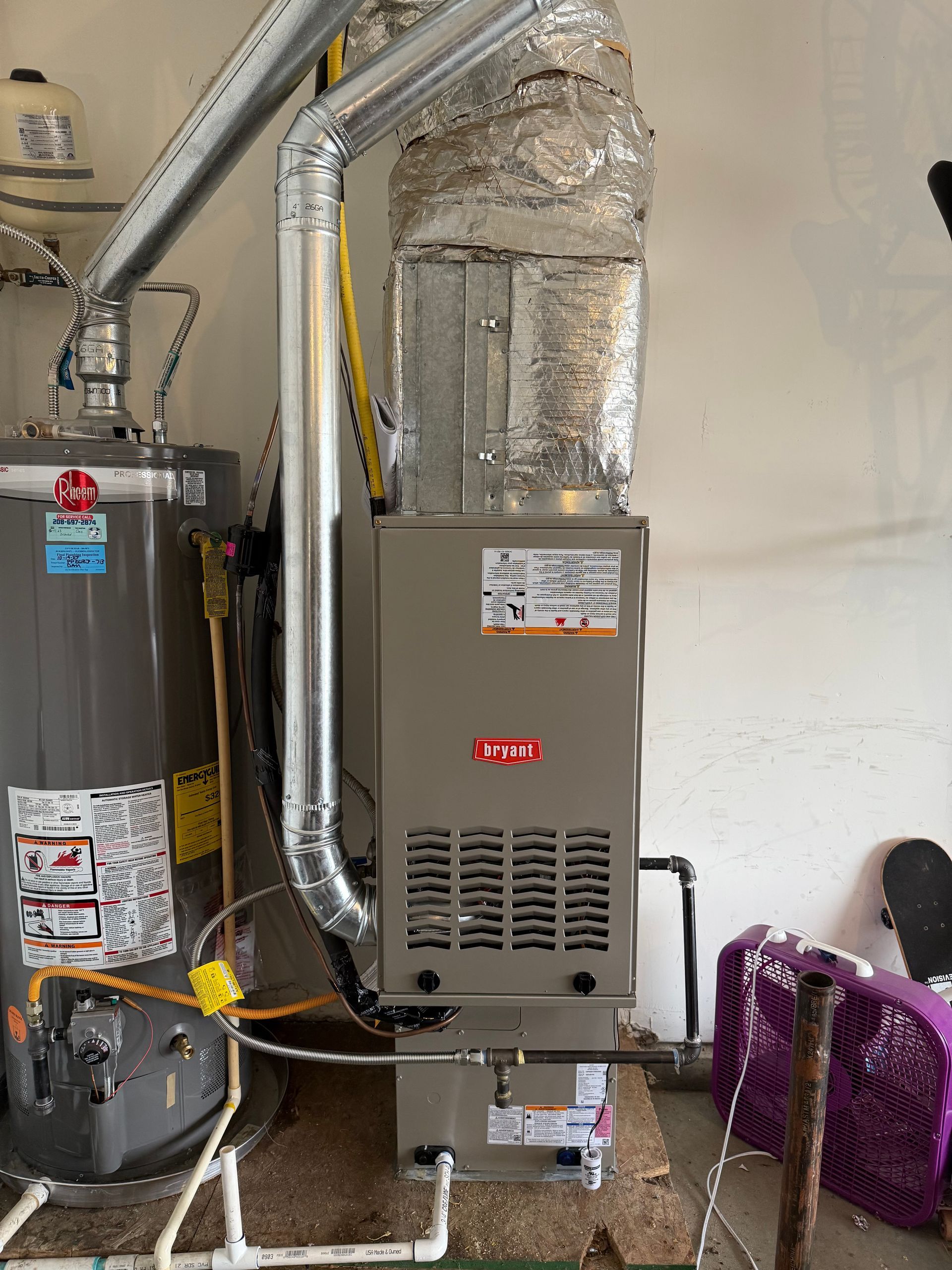 A furnace is sitting next to a water heater in a garage.
