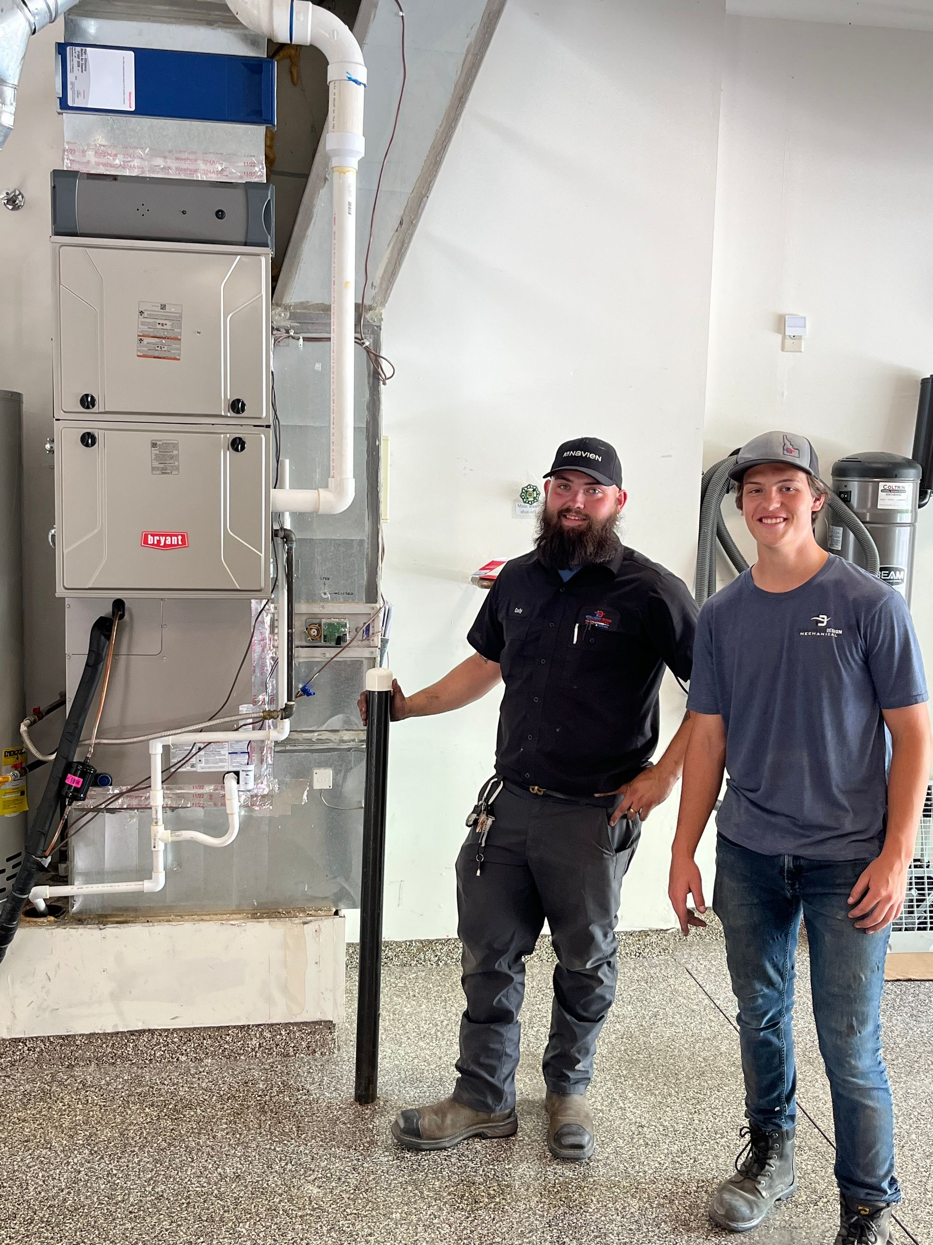 Two men are standing next to a furnace in a garage.