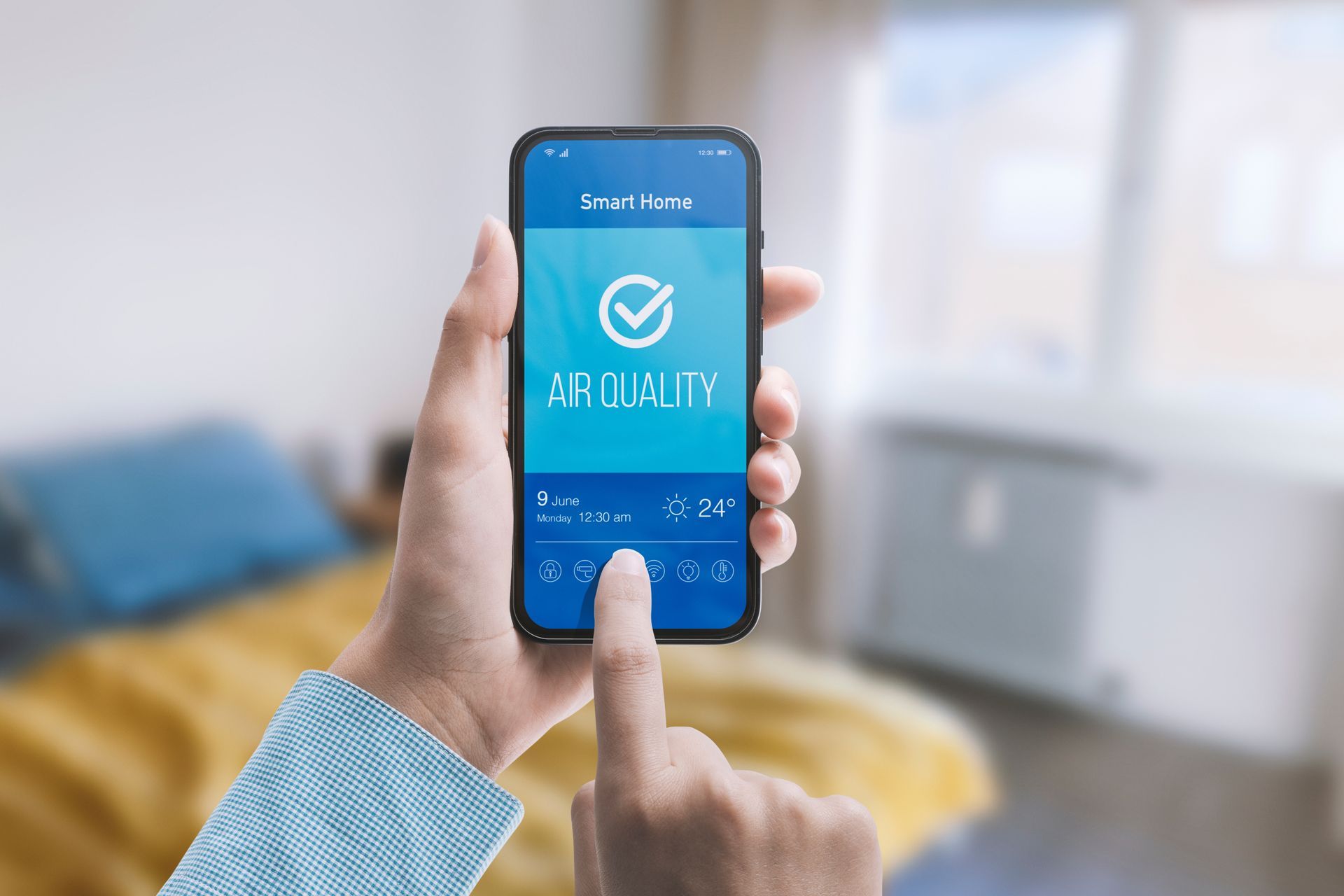 Hand holding a smartphone displaying an air quality app in a bedroom.