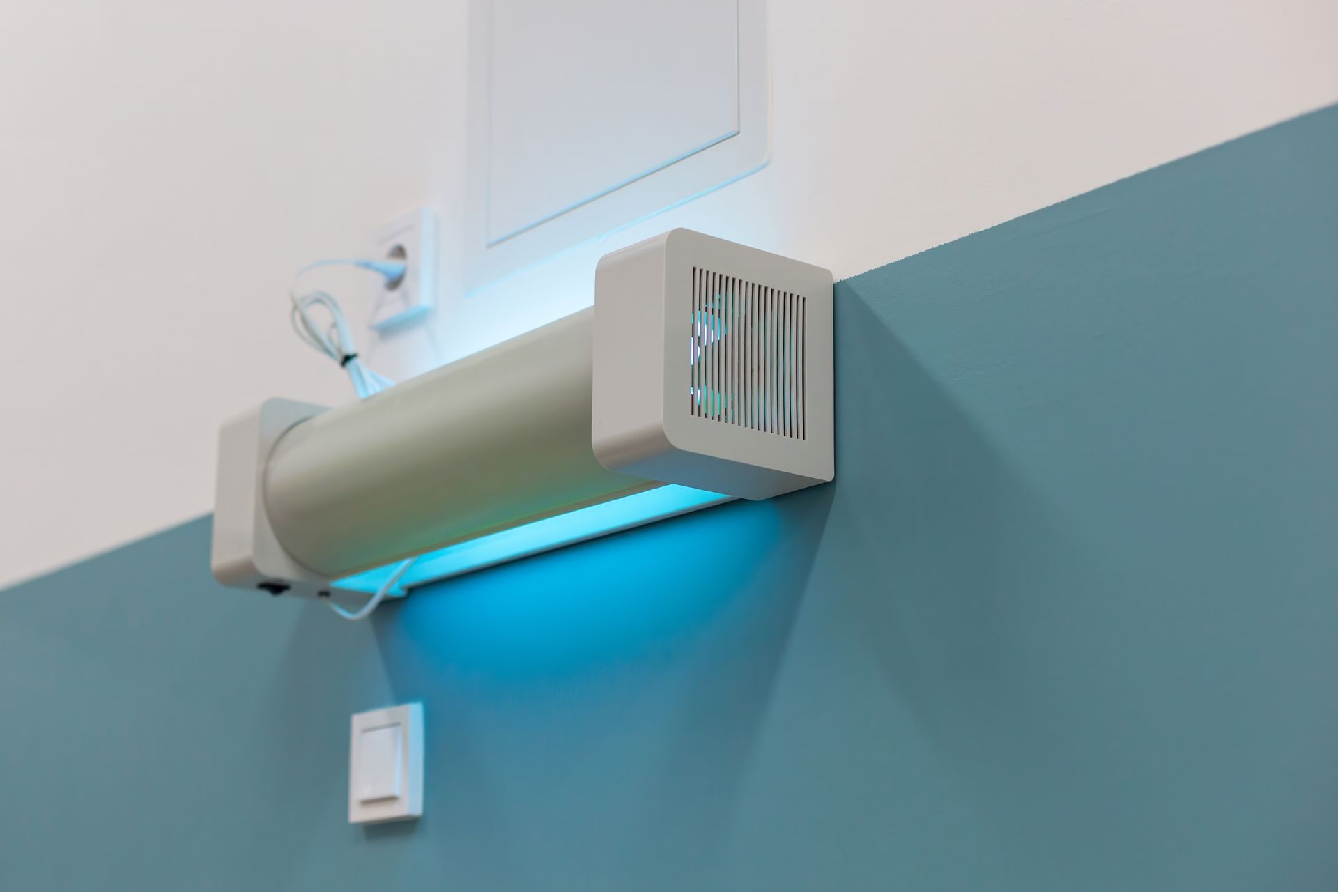 White ventilation unit on blue and white wall, emitting blue light.
