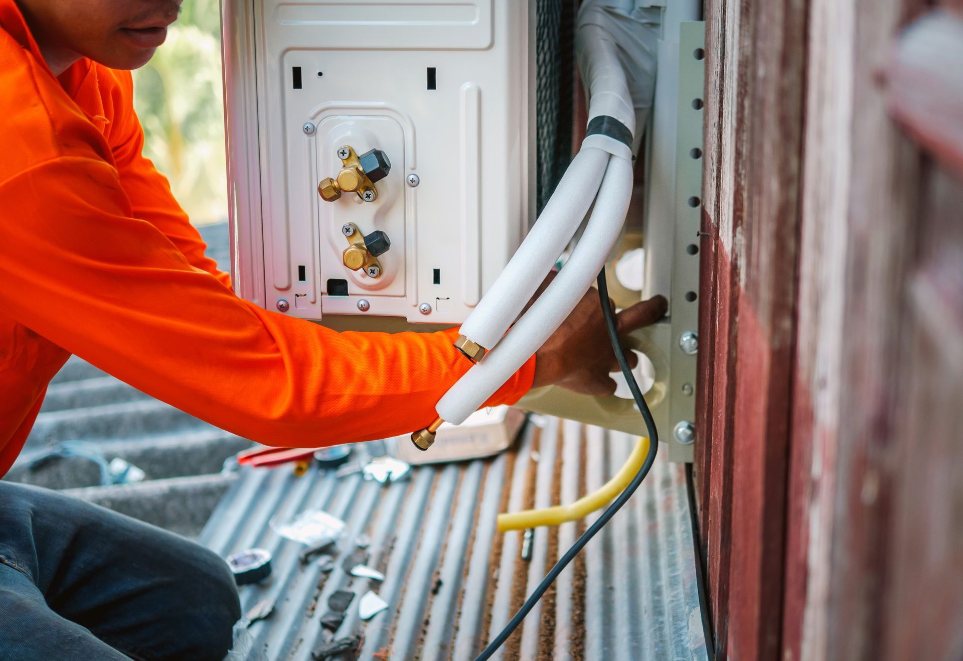 HVAC technician in orange shirt installing AC unit outside.