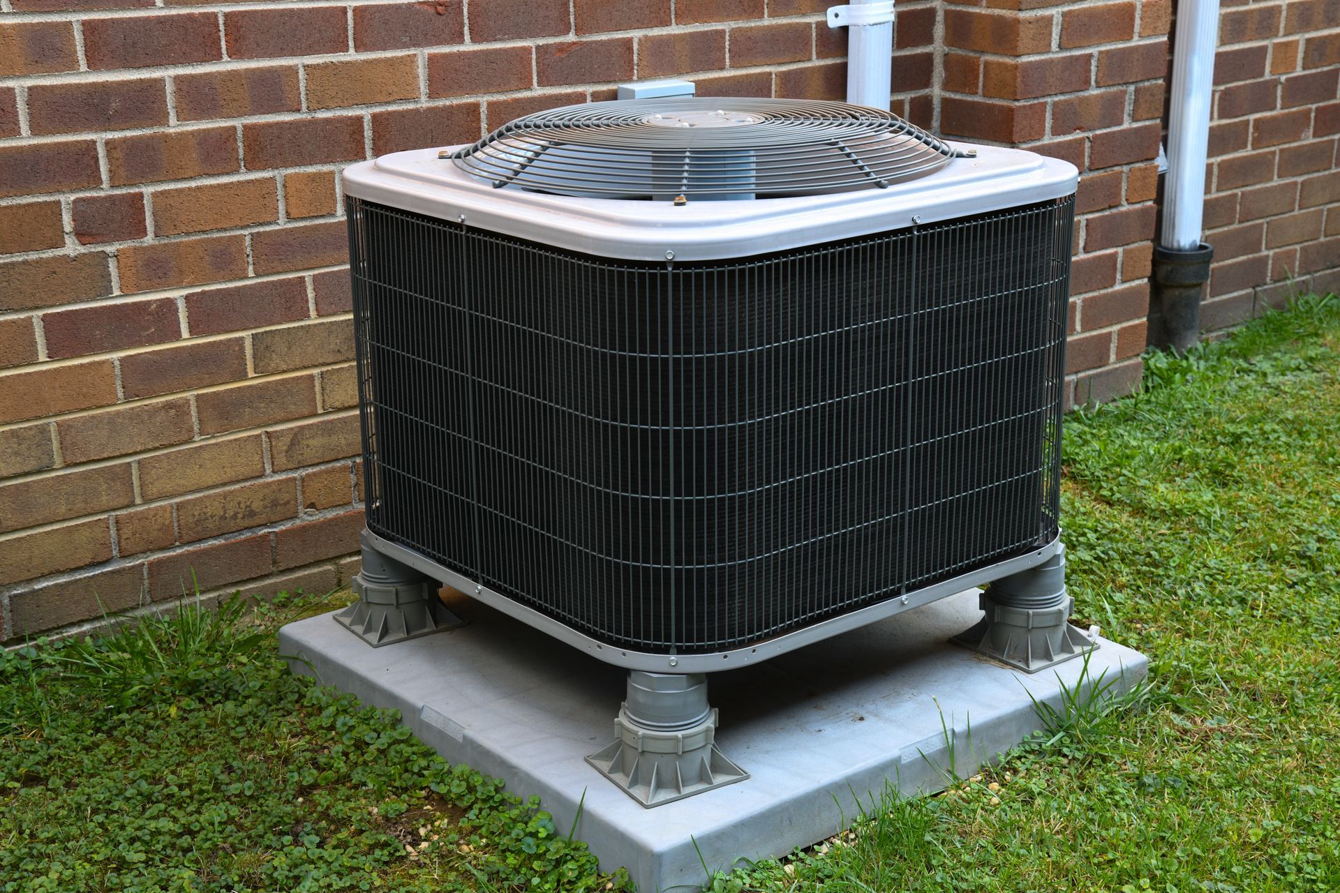 Air conditioning unit on a concrete pad near a brick wall and grass.