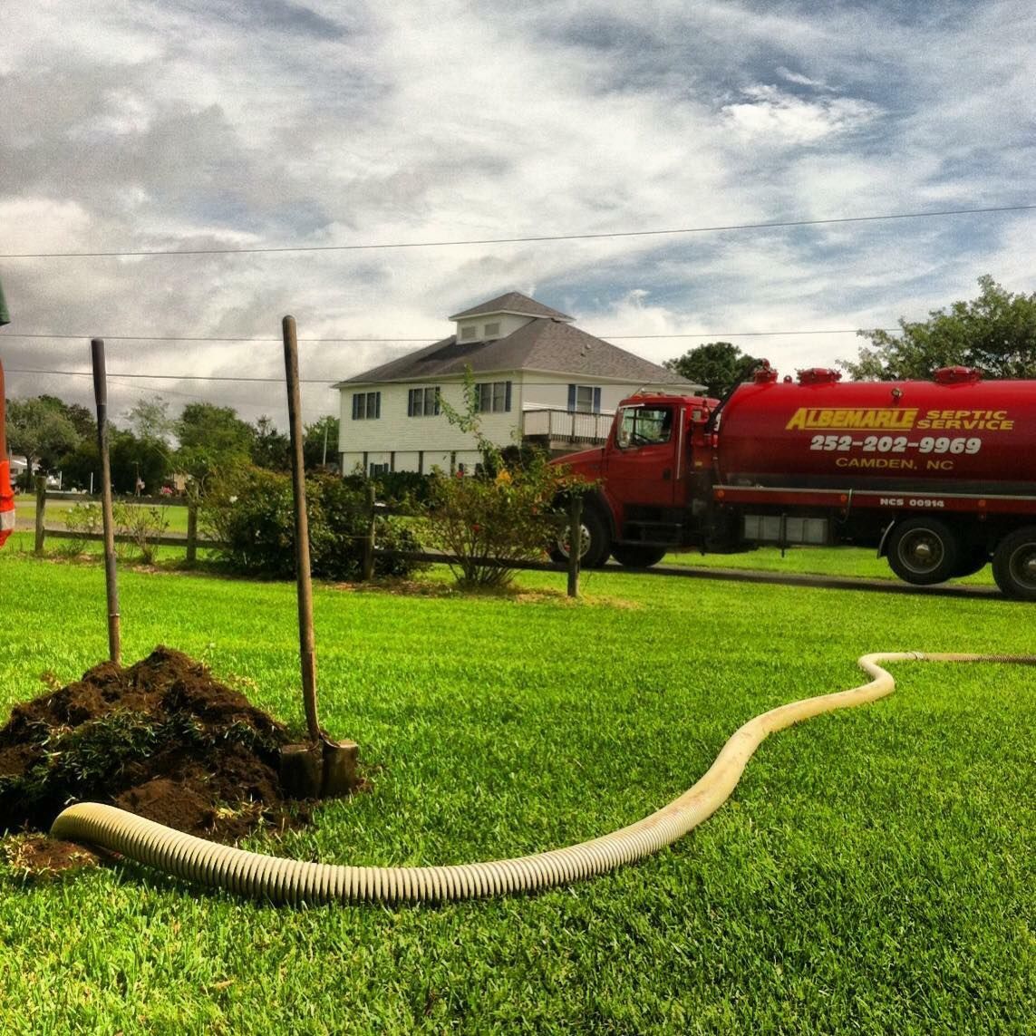 A red vacuum truck with a green hose attached to it.