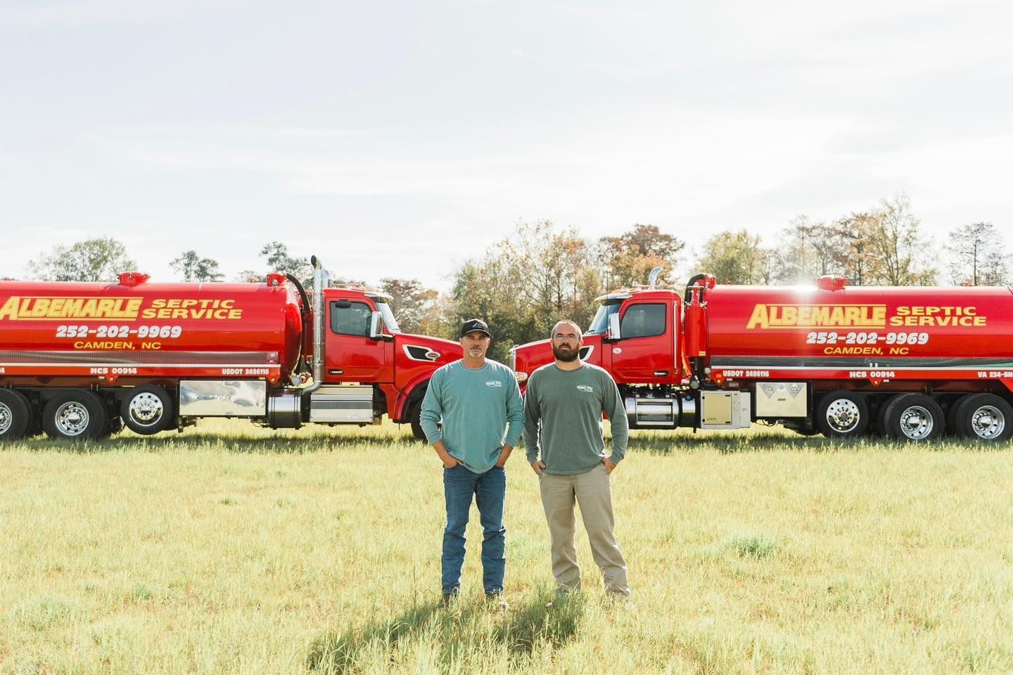 Two men are standing in a field in front of two septic tanks.