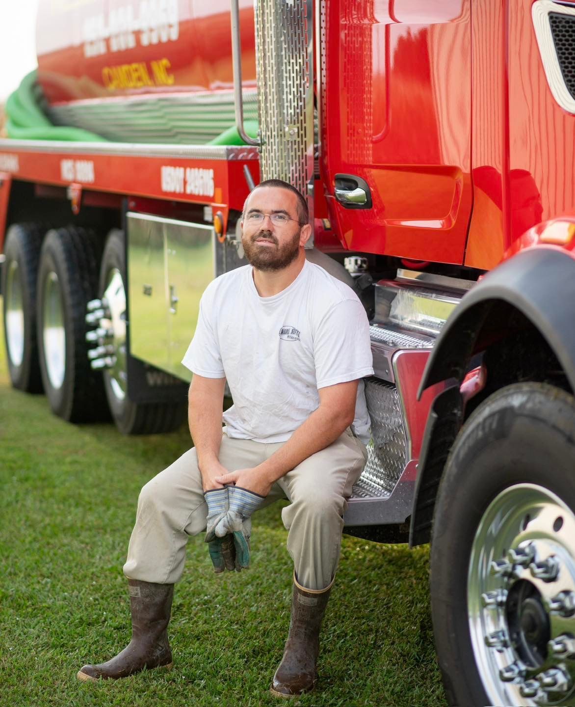 A man is standing next to a red truck with his door open.