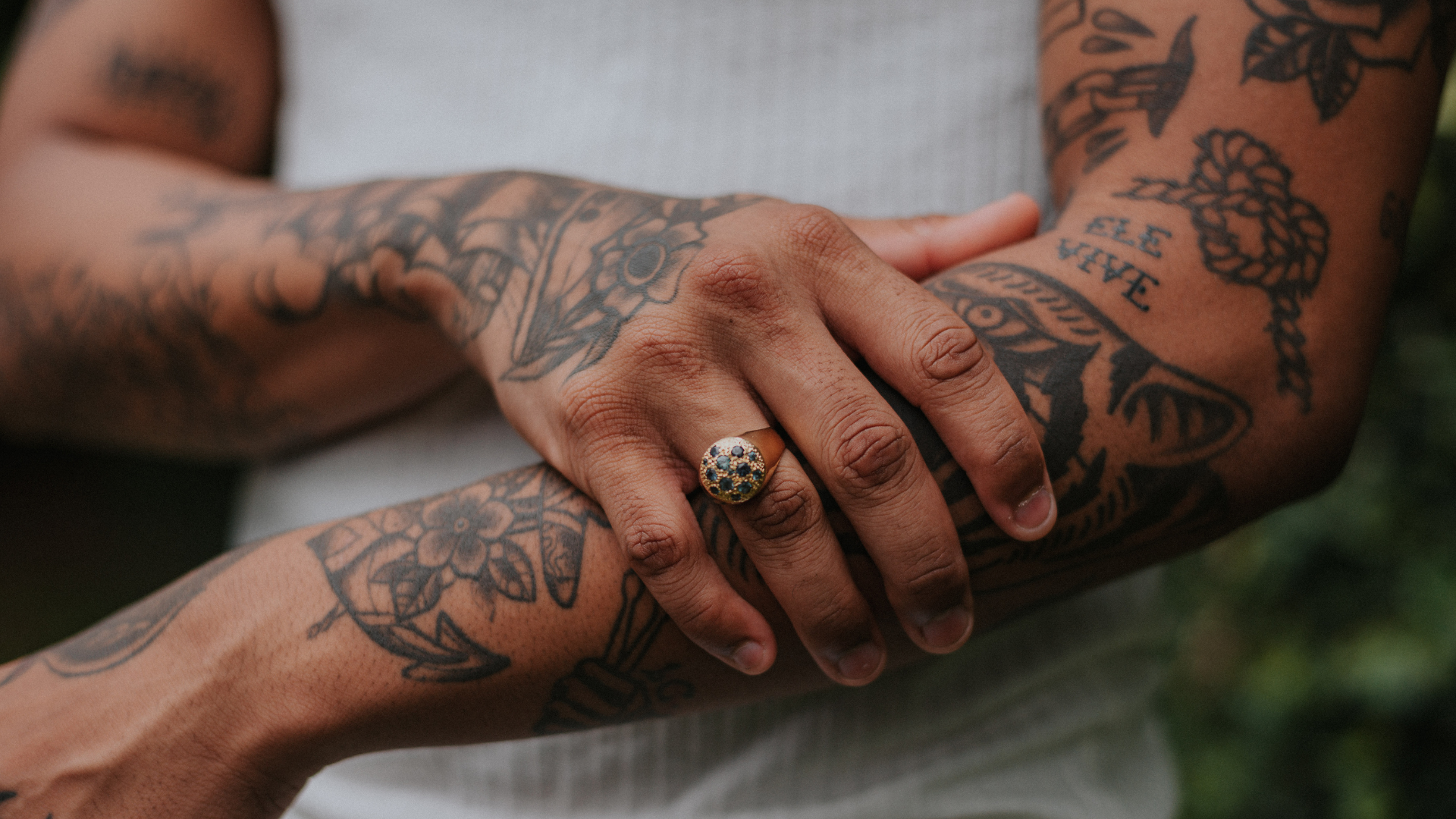 A man with a lot of tattoos on his arm is wearing a ring on his finger.