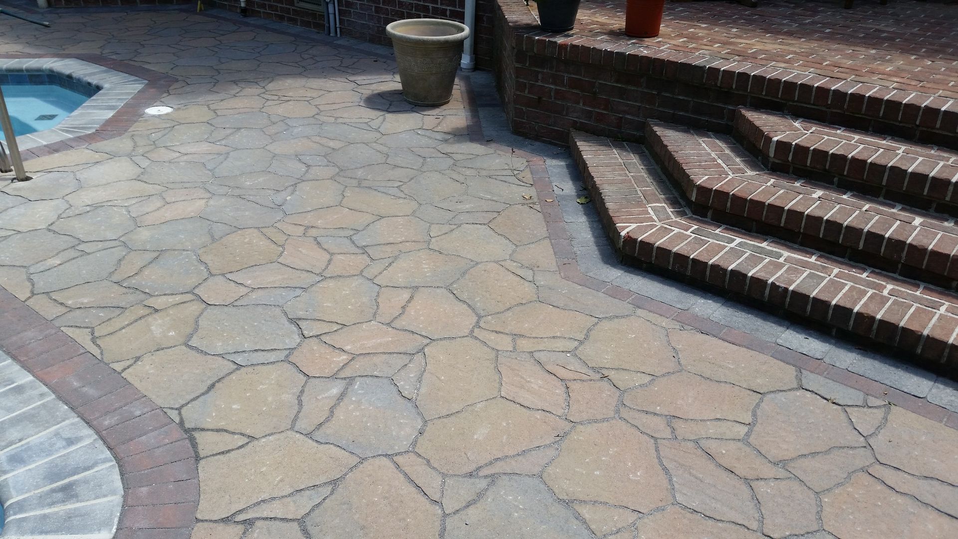 A patio with stairs and a pool in the background