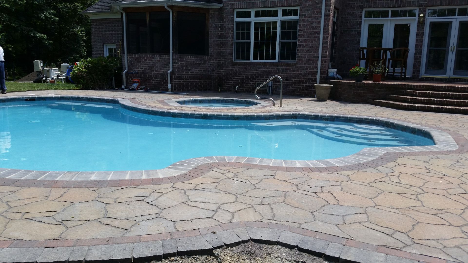 A large swimming pool with a patio in front of a brick house.