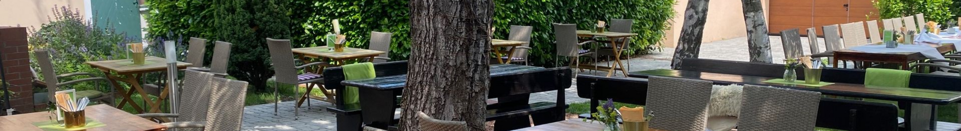 Sitzgelegenheiten im Schlossheurigen Vösendorf im Freien mit Holztischen, geflochtenen Stühlen und Bäumen, die Schatten spenden.