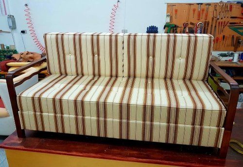 un divano con una struttura in legno e dei cuscini imbottiti in stoffa di color beige con le righe di color marrone