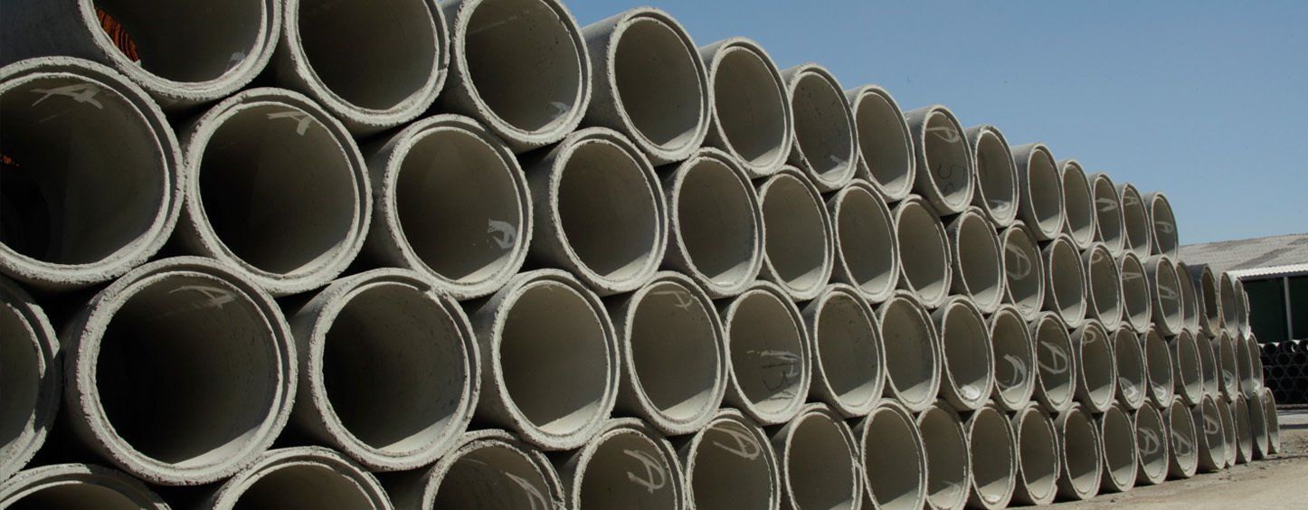 Montón de tubos de hormigón apilados al aire libre bajo un cielo azul.