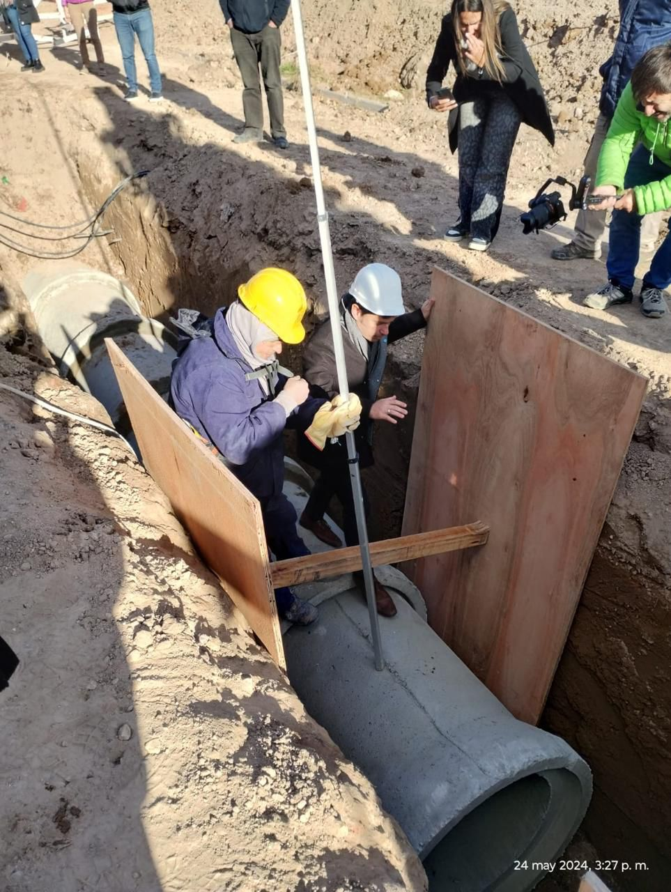 Obreros en una zanja instalando una tubería de gran tamaño, con soporte de madera contrachapada.