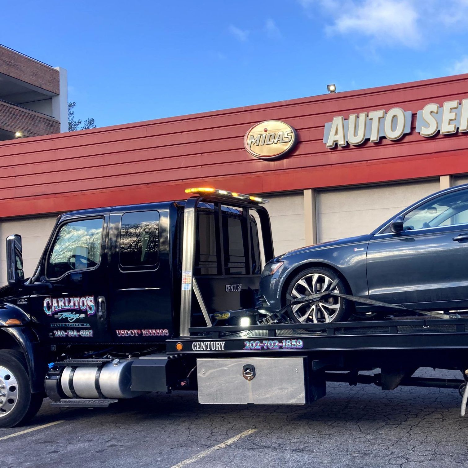 A tow truck with a car on the back is parked in front of a car dealership.