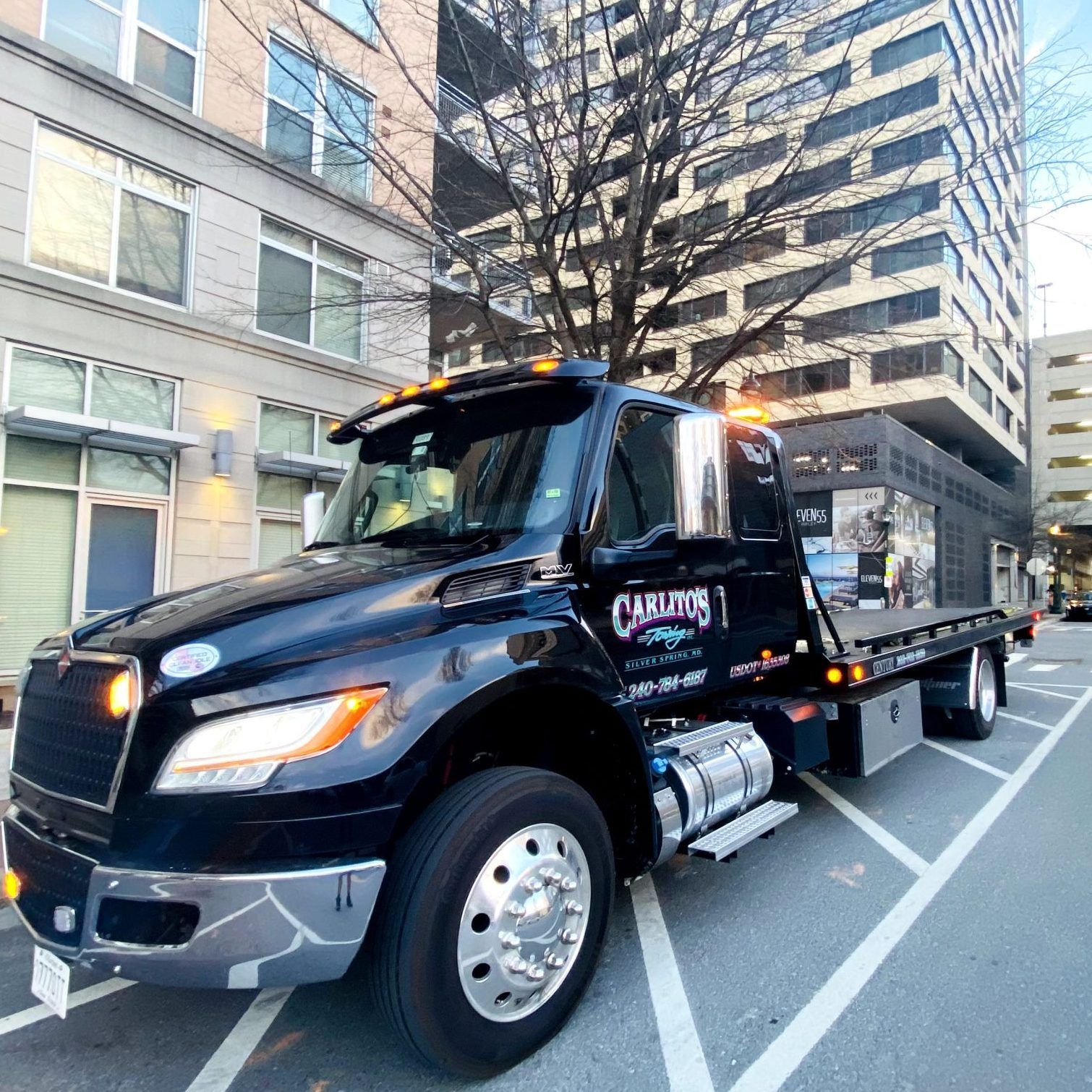 A black tow truck is parked in a parking lot in front of a building.