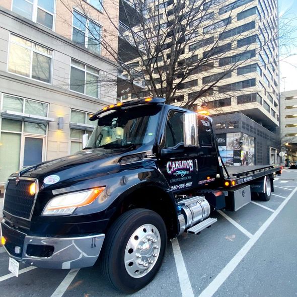 A black tow truck is parked in a parking lot in front of a building.