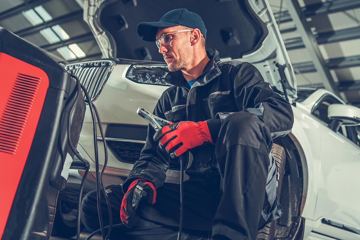 A man is sitting on the hood of a car in a garage.