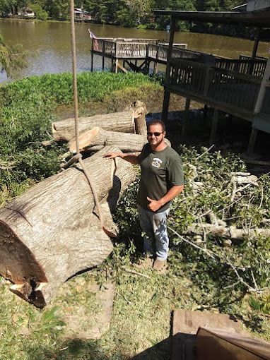 A man is standing next to a large log in the grass.