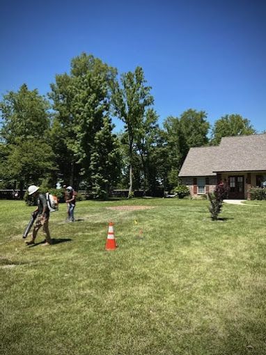 A group of people are standing in a lush green field in front of a house.