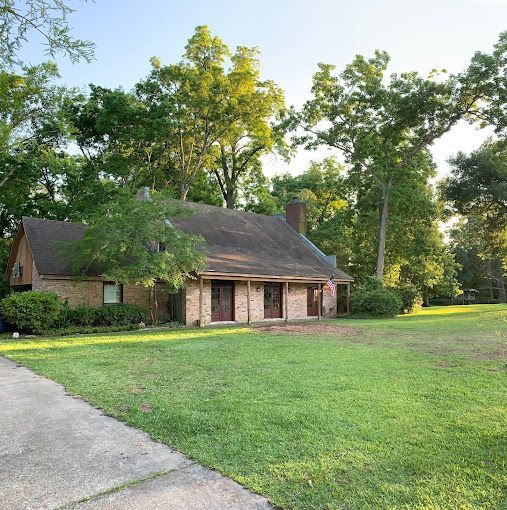 A brick house with a large lawn in front of it surrounded by trees.