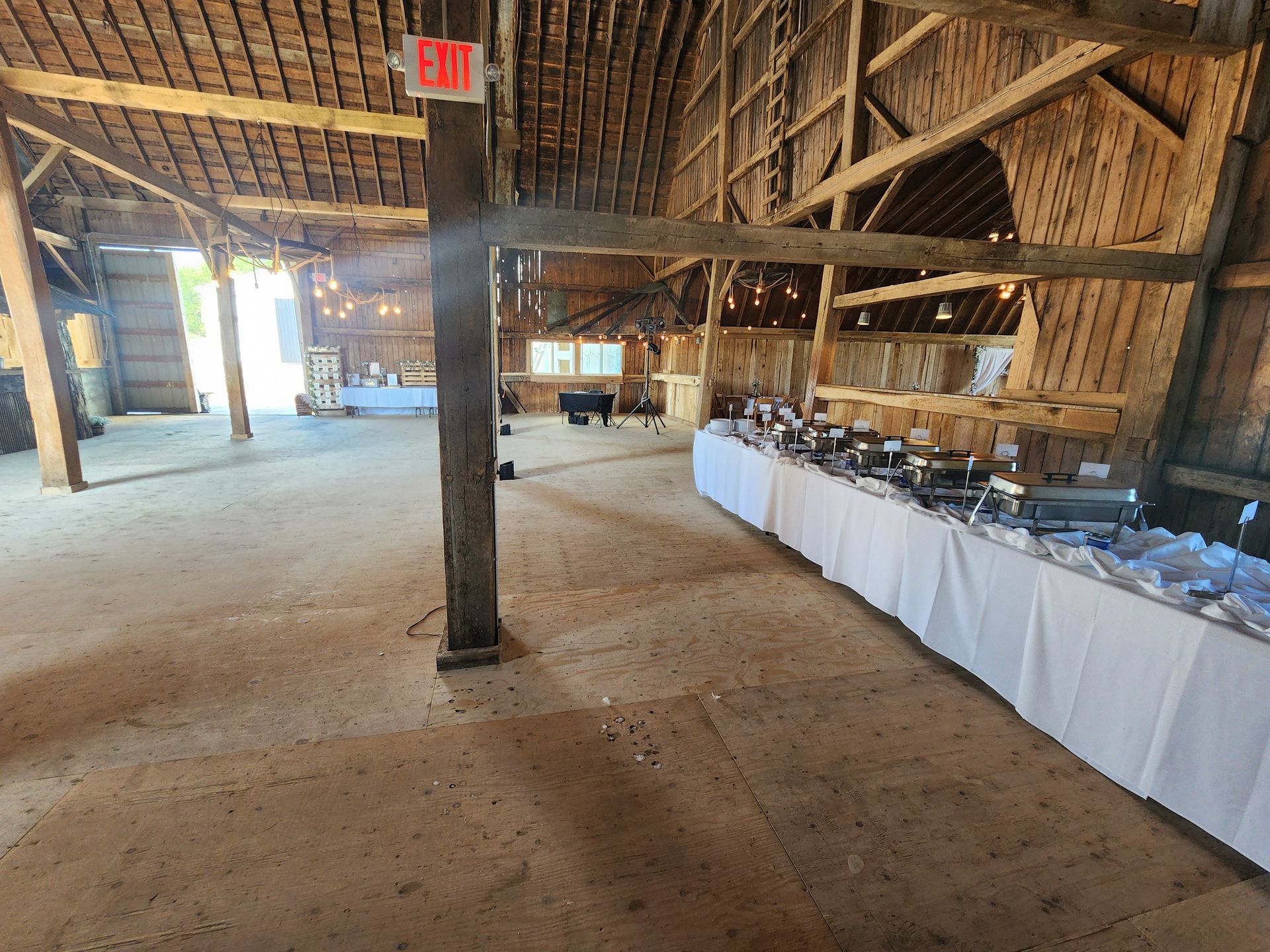 A large barn filled with tables and a red exit sign.