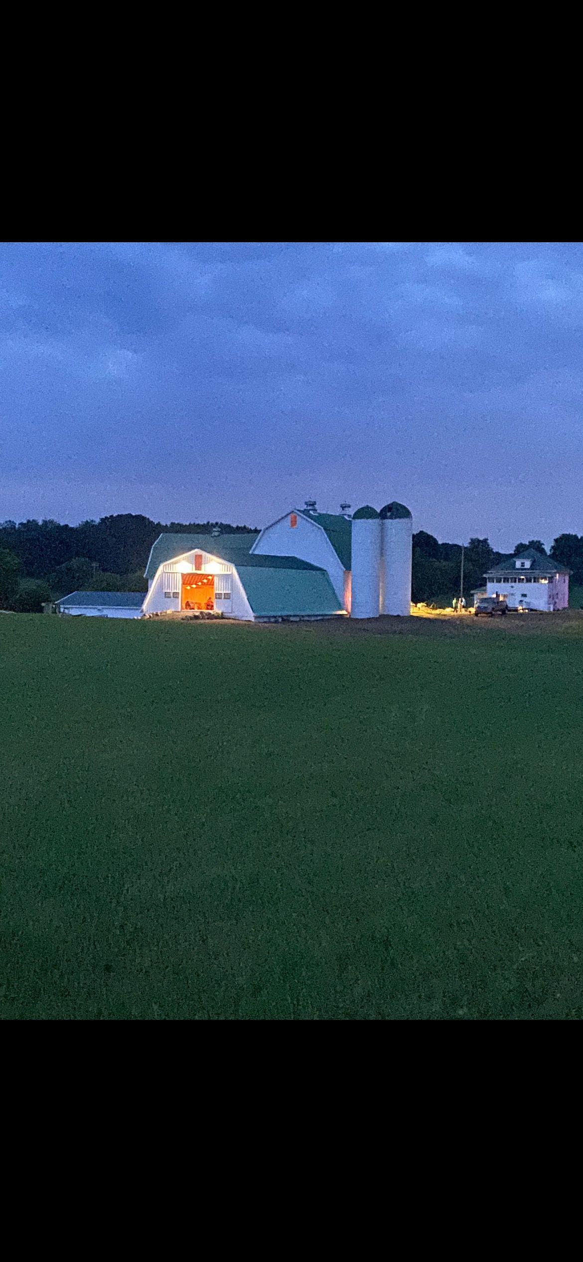 A barn is lit up in the middle of a field at night.