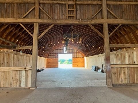 The inside of a barn with the doors open and a chandelier hanging from the ceiling.