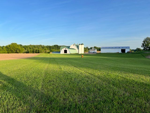 A large grassy field with a farm in the background.