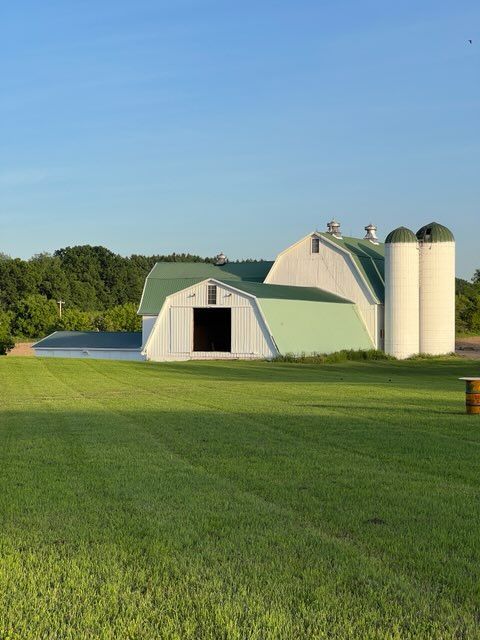 A white barn with a green roof sits in the middle of a grassy field.