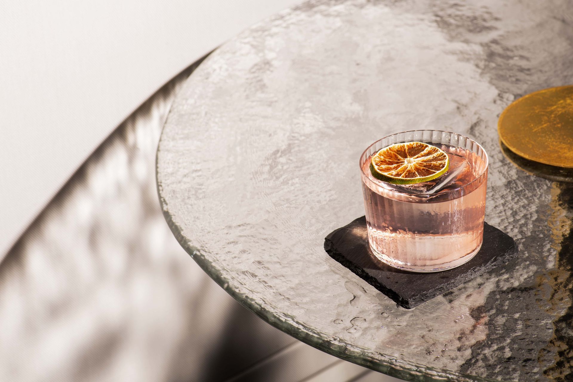 A glass of pink liquid with a slice of orange on a table.