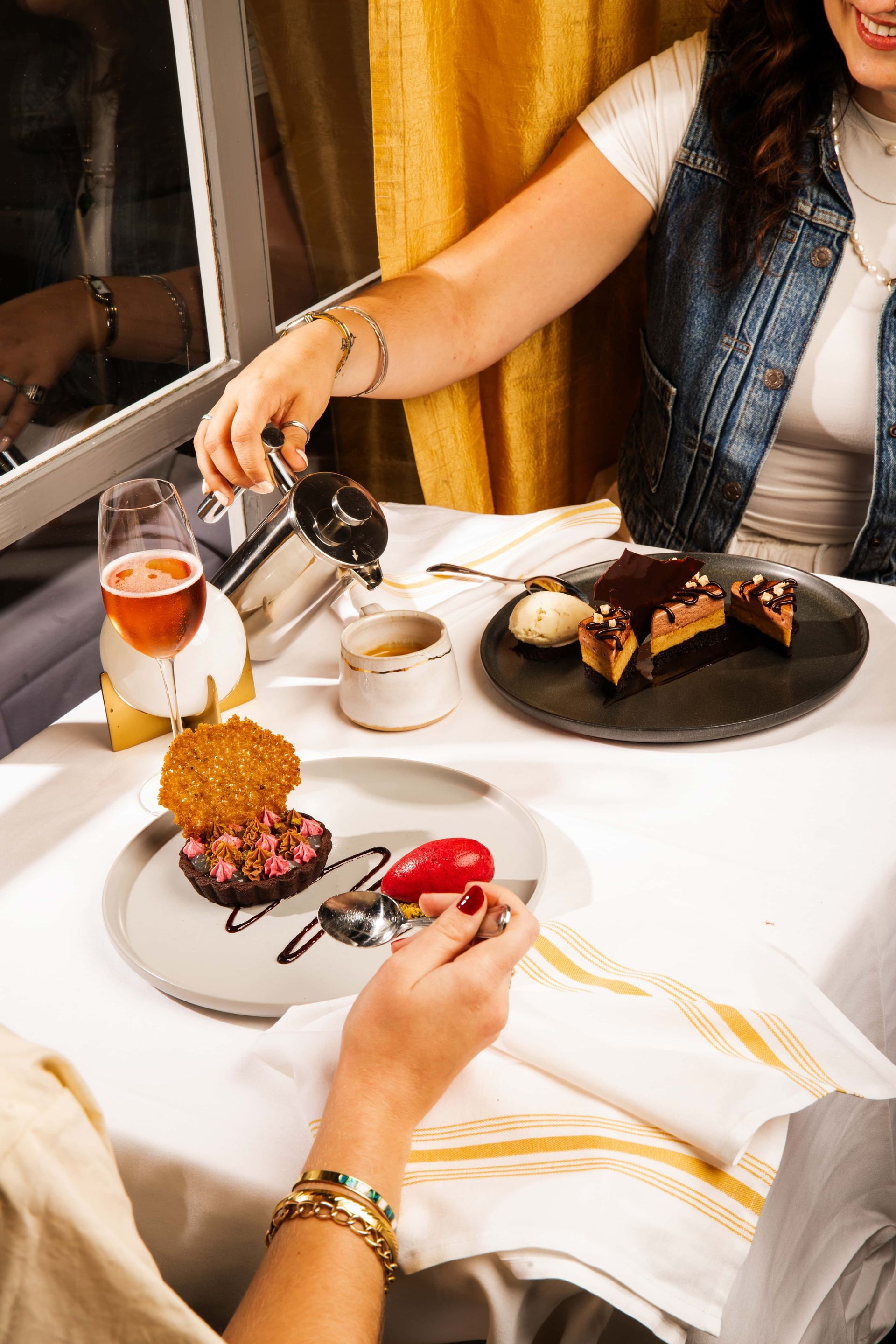 A woman is pouring wine into a glass while sitting at a table with plates of food.