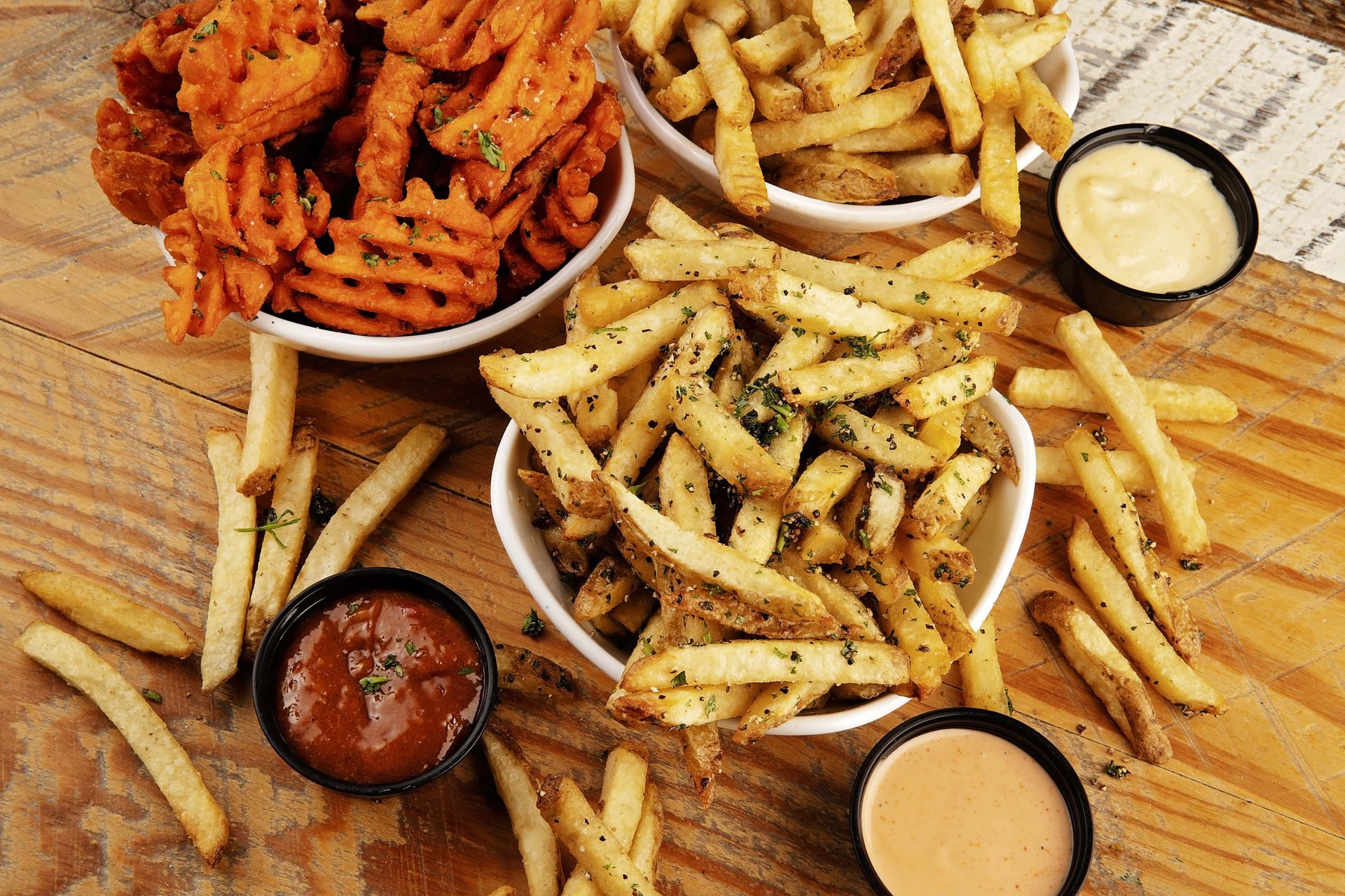 A wooden table topped with bowls of french fries and dipping sauces.