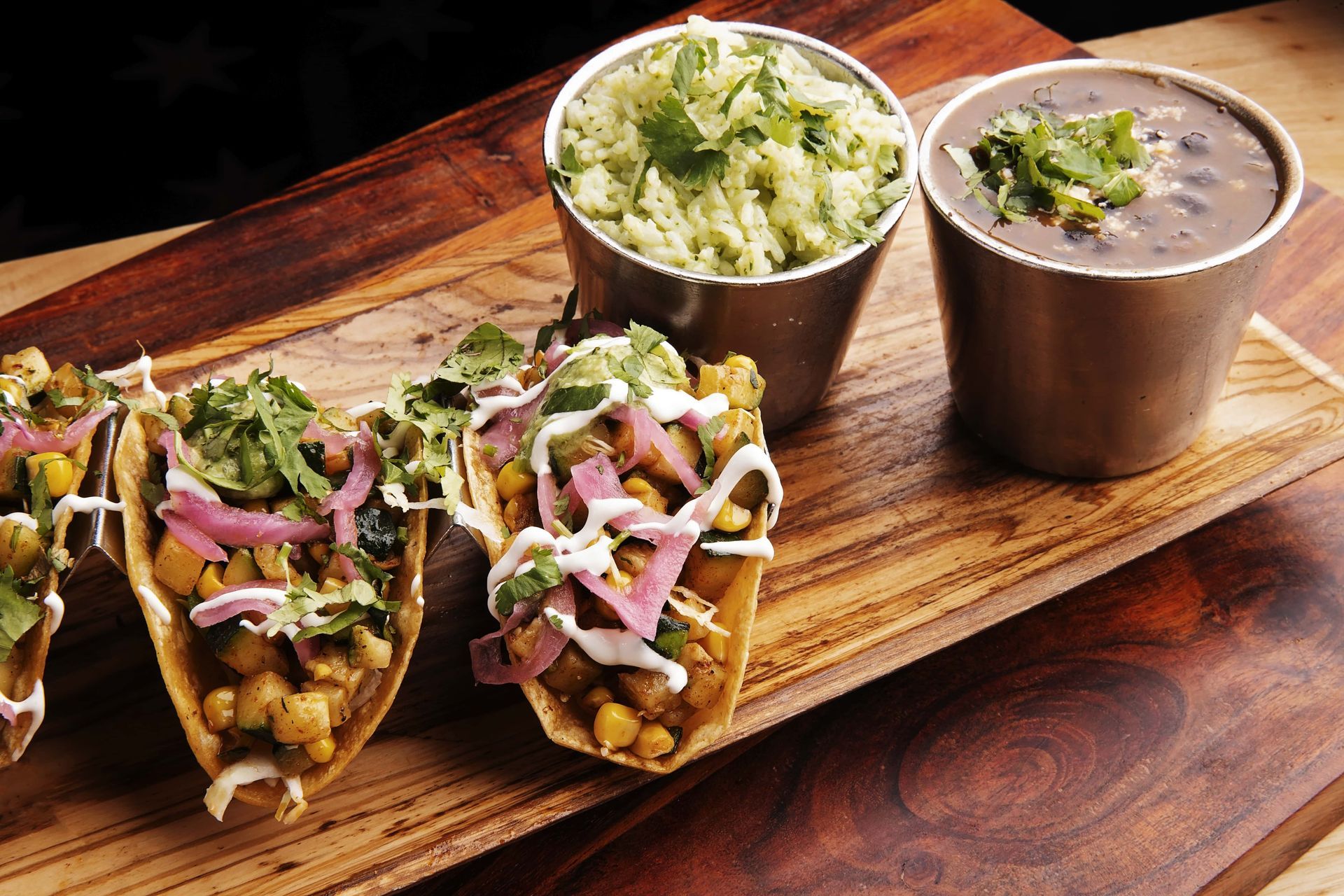 A wooden tray with tacos , rice and beans on it