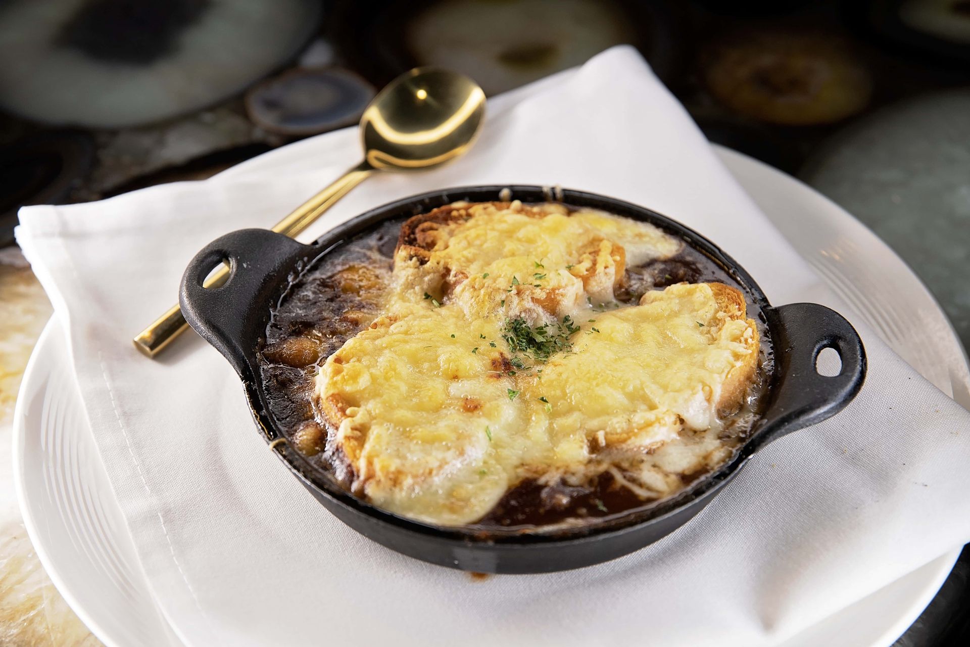 A bowl of french onion soup with a spoon on a plate.